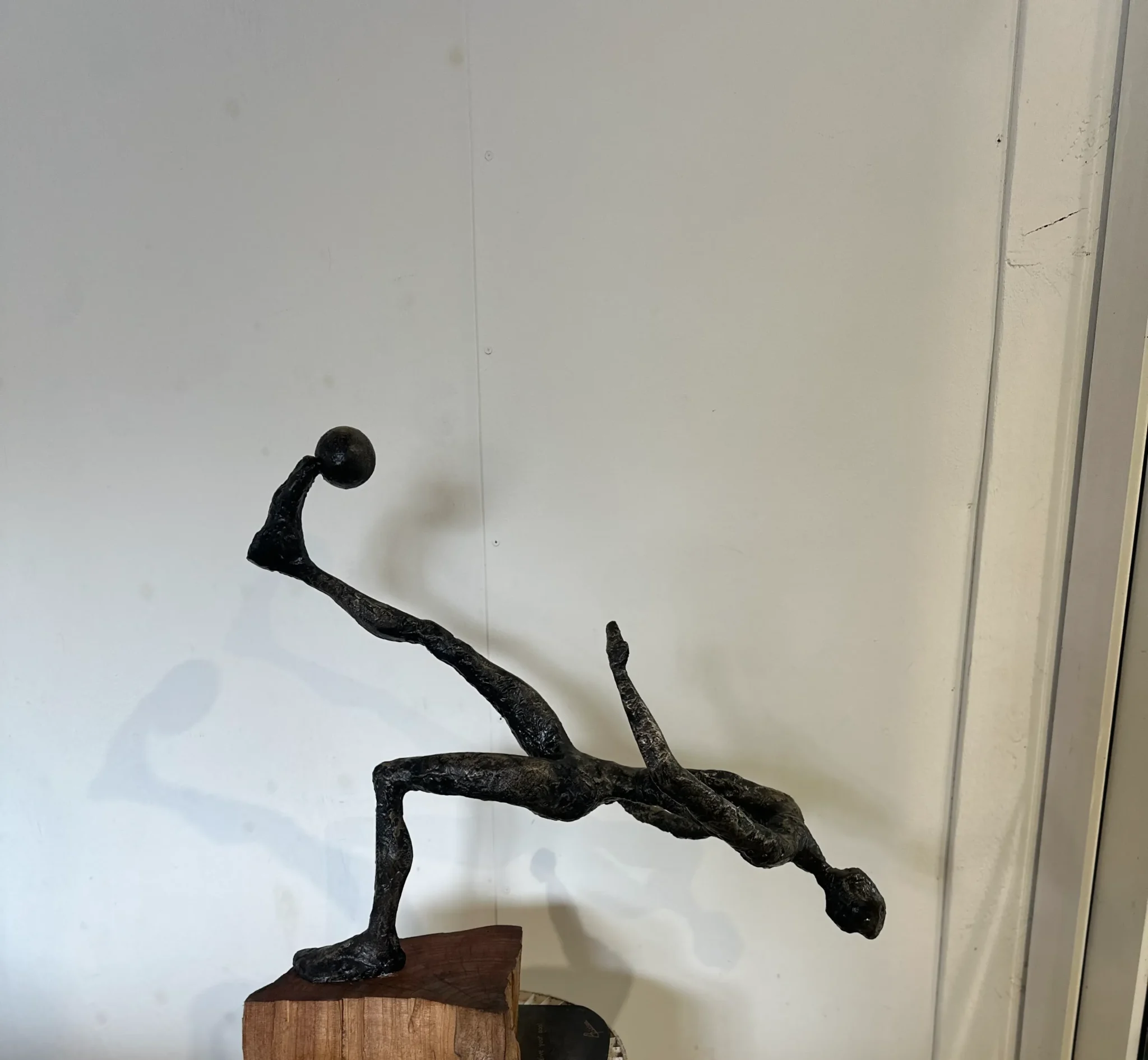 a black clay sculpture of a body leaning backwards kicking a football